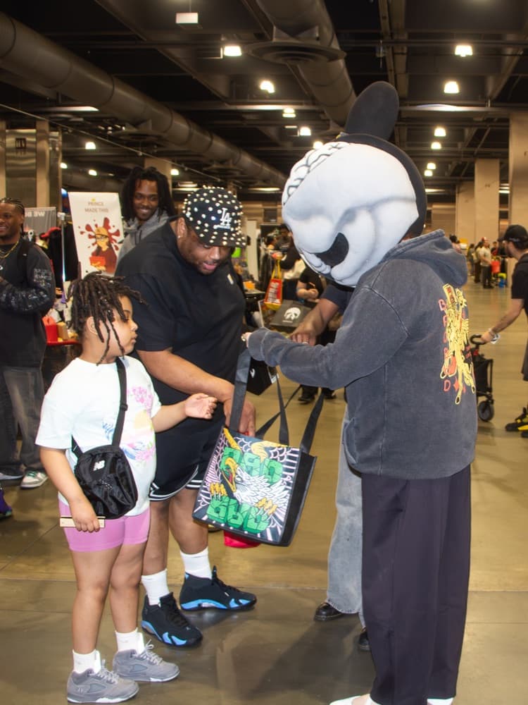 A costumed mascot handing a tote bag to a family on an expo floor